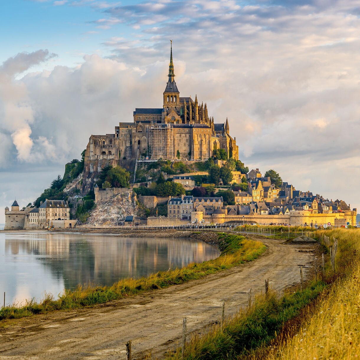 Mont Saint-Michel perched on a rocky island in Normandy, France, with its abbey towering over stone houses and green tidal flats under a bright blue sky.